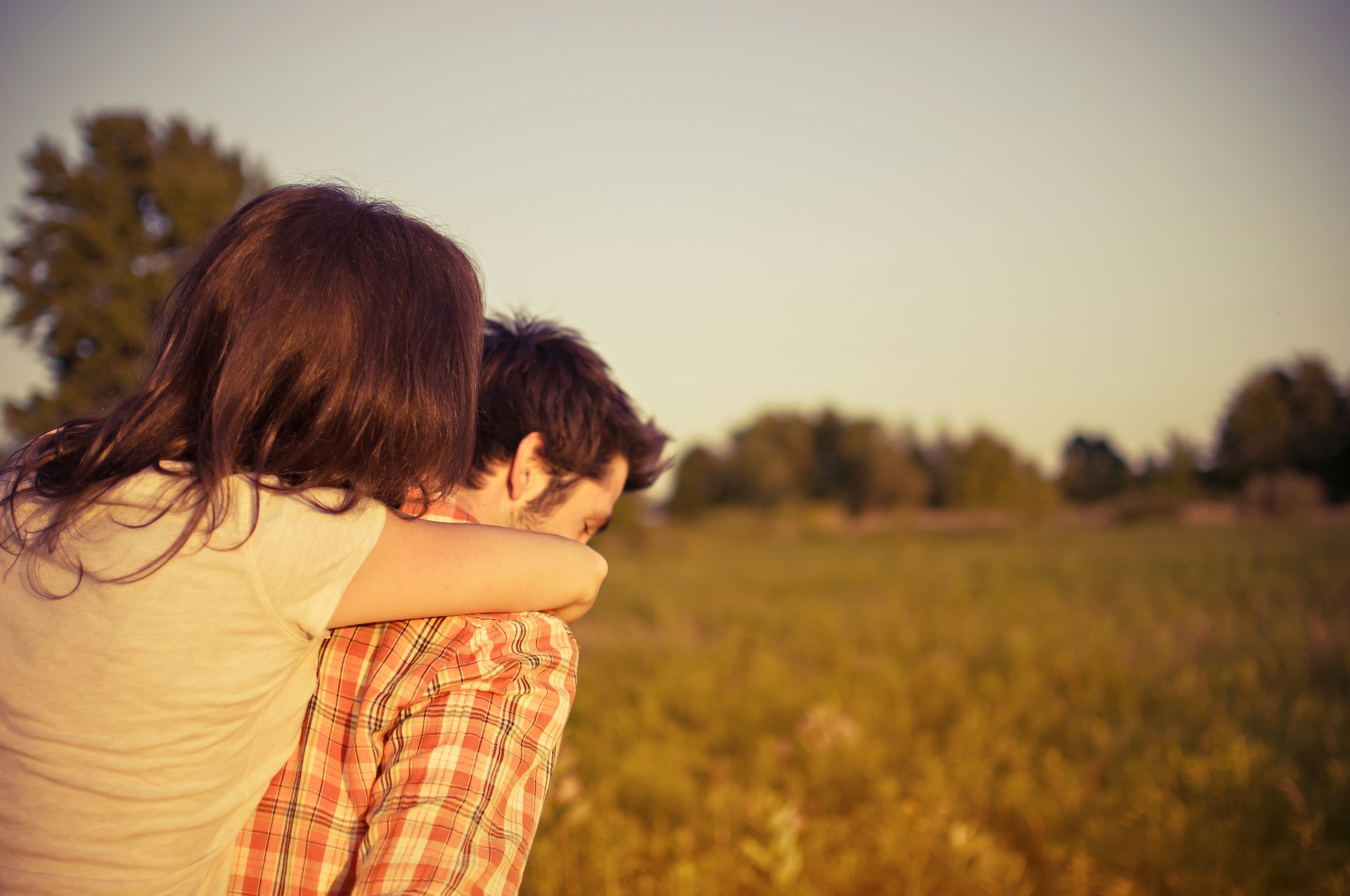 Woman embracing man in a field at sunset.