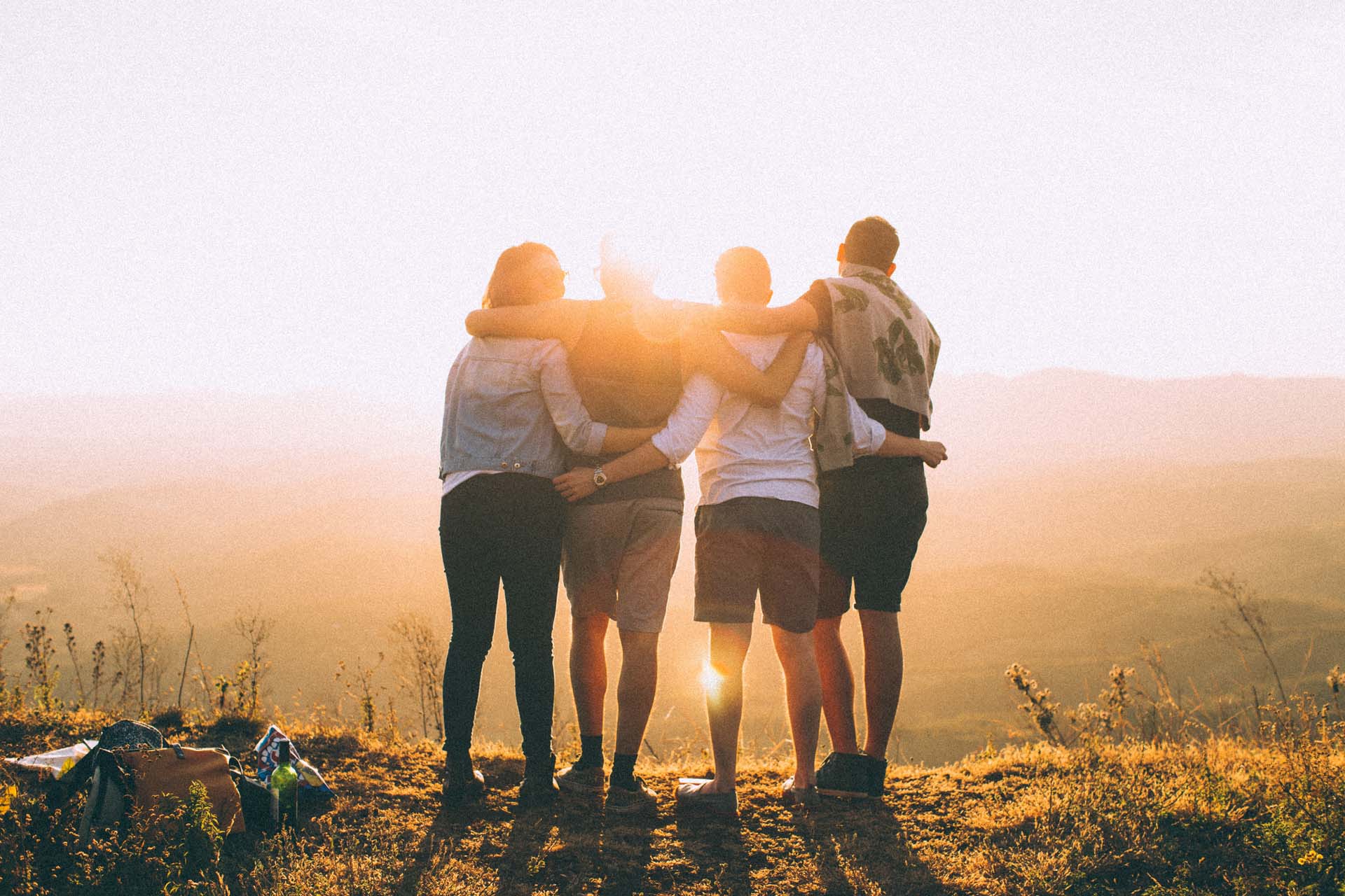 Four friends embrace on a hilltop at sunset.