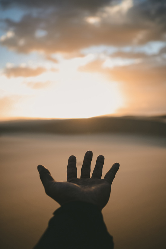 hand reaching towards sunrise on beach