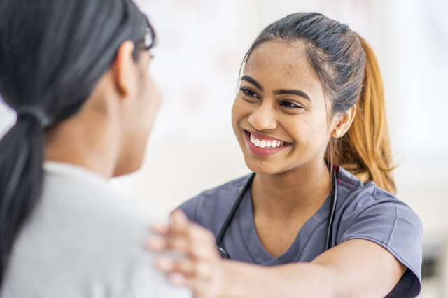 A smiling nurse in scrubs places a comforting hand on a patient's shoulder.